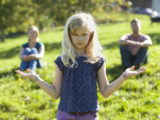 une jeune fille à l'air sérieux ouvre les paumes de ses mains comme dans un geste de choix difficile entre deux possibilités, au-dessus de ses mains on voit au loin, flous, un homme et une femme qui semblent être ses parents.