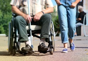 un homme en fauteuil roulant et une jeune personne marchant à côté (le cadrage ne montre que leurs jambes)