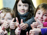 un groupe de jeunes filles alignées regardent la caméra, sourient et lèvent le pouce dans un signe positif