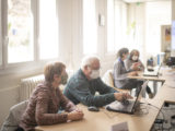 par groupes de deux, les participants de l'atelier numérique s'exercent : on voit un homme taper sur son clavier tandis que sa coéquipière l'observe.