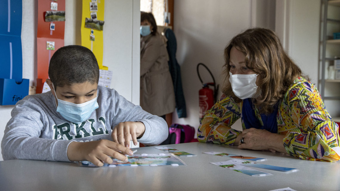 Un enfant joue avec des cartes tandis qu'une dame l'observe et l'accompagne.