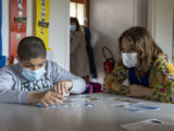 Un enfant joue avec des cartes tandis qu'une dame l'observe et l'accompagne.