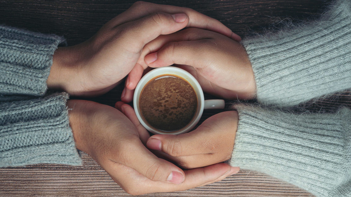 deux personnes tiennent une tasse de café entre leurs mains enlacées. l'une semble soutenir l'autre.