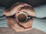 deux personnes tiennent une tasse de café entre leurs mains enlacées. l'une semble soutenir l'autre.