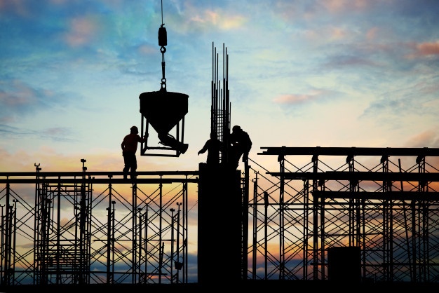 contre-jour devant un ciel coloré, des silhouettes travaillant en haut d'une structure de chantier