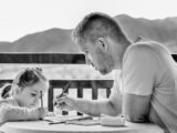 Sur un balcon, un père s'occupe de sa petite fille en dessinant avec elle.