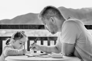 Sur un balcon, un père s'occupe de sa petite fille en dessinant avec elle.