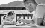 Sur un balcon, un père s'occupe de sa petite fille en dessinant avec elle.