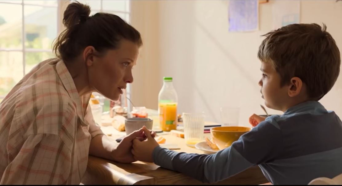 Image extraite du film "La vraie famille", la mère d'accueil tient la main du garçon lors d'un petit déjeuner.