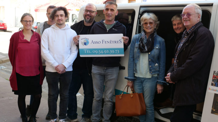 un groupe de personnes se tiennent devant un van, et tiennent une pancarte où on peut lire "Asso FenêtreS, tel 09 54 92 39 73"