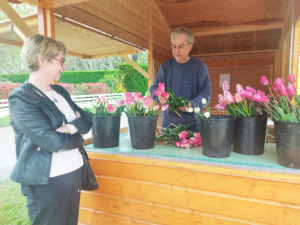 Une donatrice est en train de choisir son bouquet de tulipes sur un stand extérieur en bois, un homme s'occupe de les trier et d'encaisser les dons.
