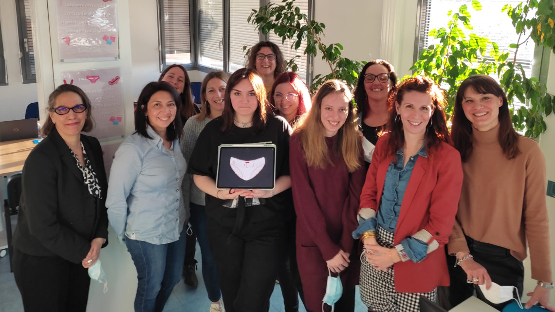 un groupe de femmes impliquées dans le Collectif Menstru'eLles pose pour la photo , la graphiste, devant au centre, tient une tablette avec le logo représentant une menstruelle rose