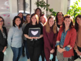 un groupe de femmes impliquées dans le Collectif Menstru'eLles pose pour la photo , la graphiste, devant au centre, tient une tablette avec le logo représentant une menstruelle rose