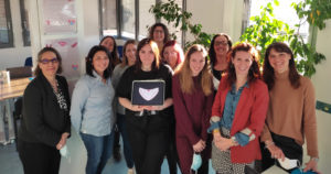 un groupe de femmes impliquées dans le Collectif Menstru'eLles pose pour la photo , la graphiste, devant au centre, tient une tablette avec le logo représentant une menstruelle rose
