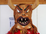 Une personne porte un masque de "monstre", poilu, cornu et avec de grandes dents pointues, pour le projet Festum