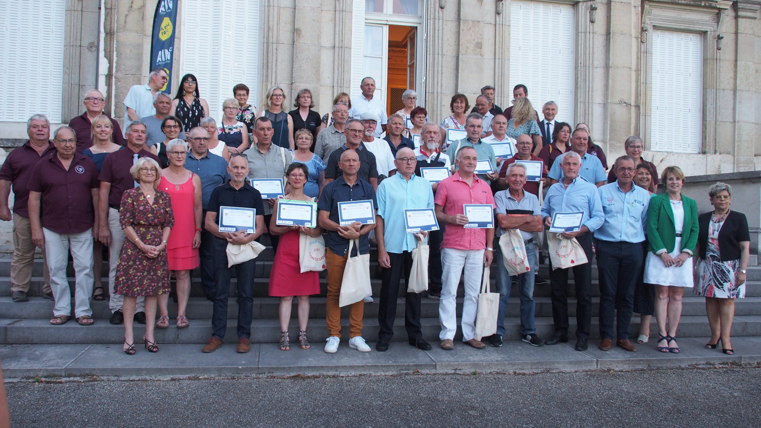 Devant les bâtiments du Département, un groupe de donneurs et organisateurs posent pour une photo. les donneurs montrent leur diplôme reconnaissant leur effort exceptionnel de dons de sang.