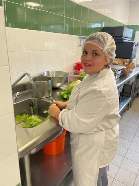 Une jeune cuisinière sourit devant l'évier où elle prépare et nettoie la laitue