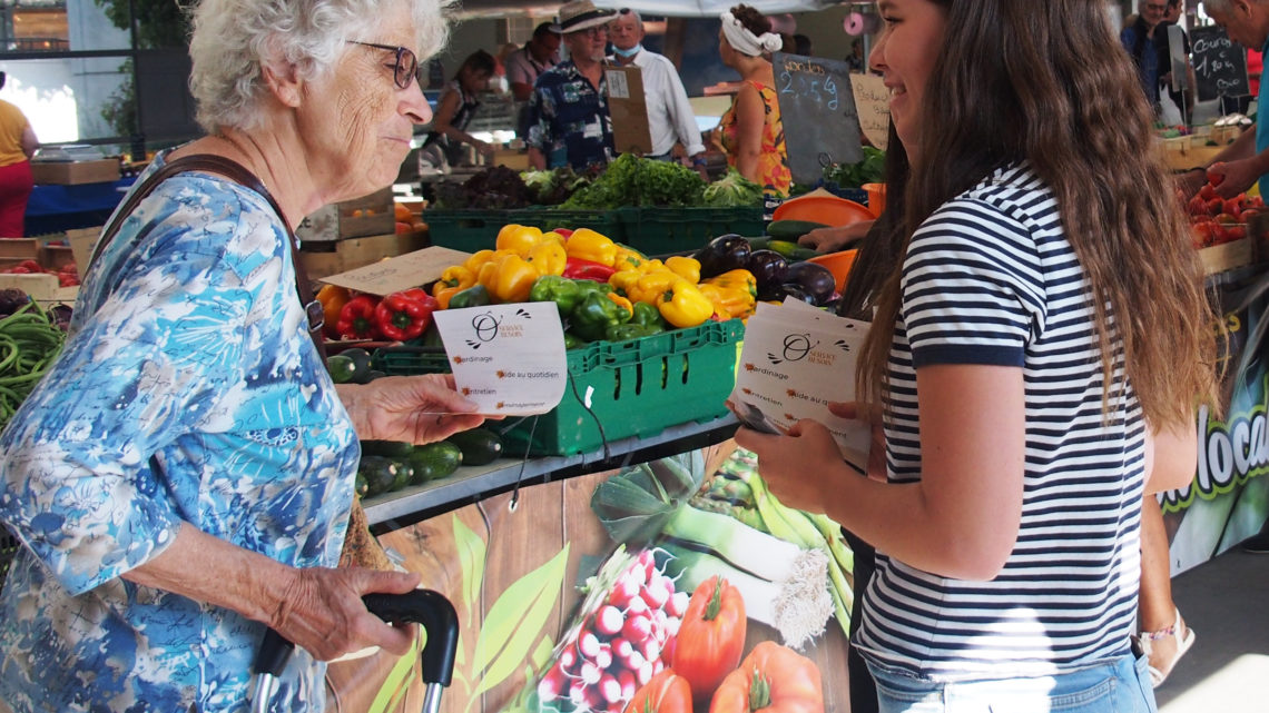 Une jeune fille distribue des flyers au marché de Bourg en Bresse, elle le donne à une dame âgée devant les étals d'un primeur.