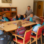 Atelier Adapa : des personnes âgées sont réunies autour d'une table avec 6 enfants et jouents ensemble à un jeu de société