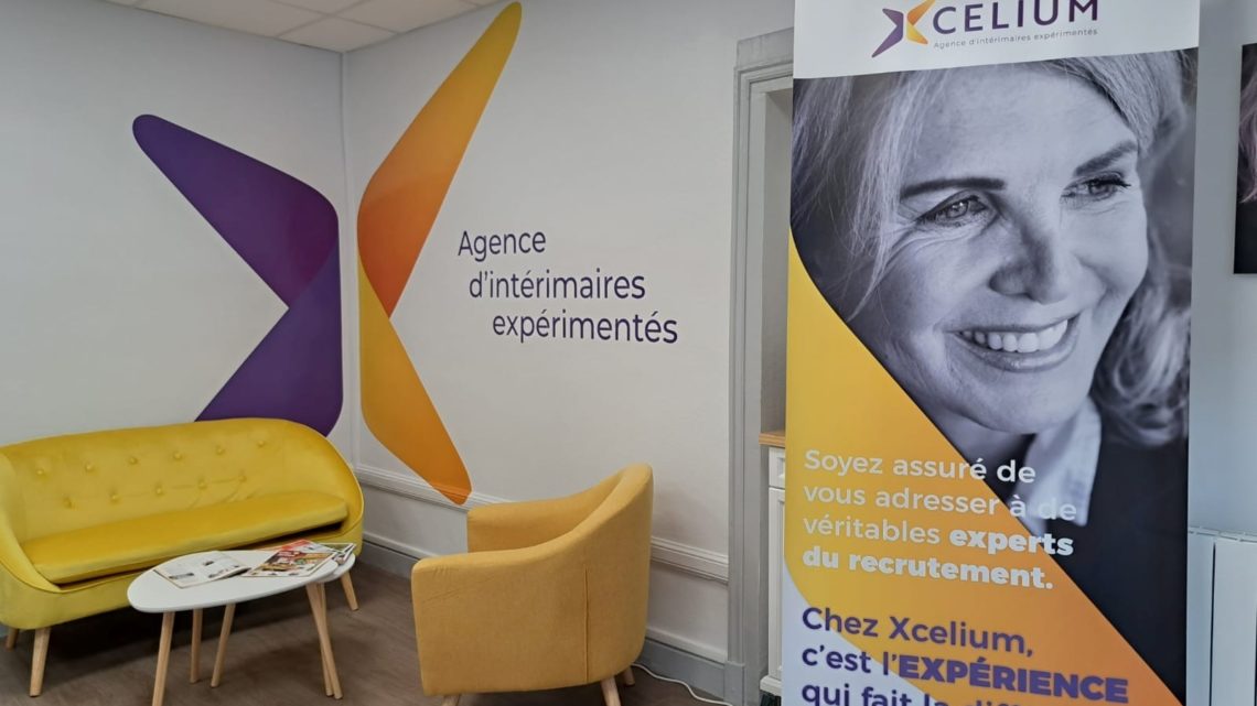 Locaux d'Xcelium : à l'intérieur, un bâtiment entièrement rénové et moderne avec un coin convivial (fauteuil, canapé,) et des éléments de décoration murale / roll-up aux couleurs de l'agence : violet et jaune.