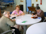 Trois dames sont autour d'une table, en train d'écrire sur leur carnet respectif.