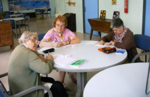 Trois dames sont autour d'une table, en train d'écrire sur leur carnet respectif.