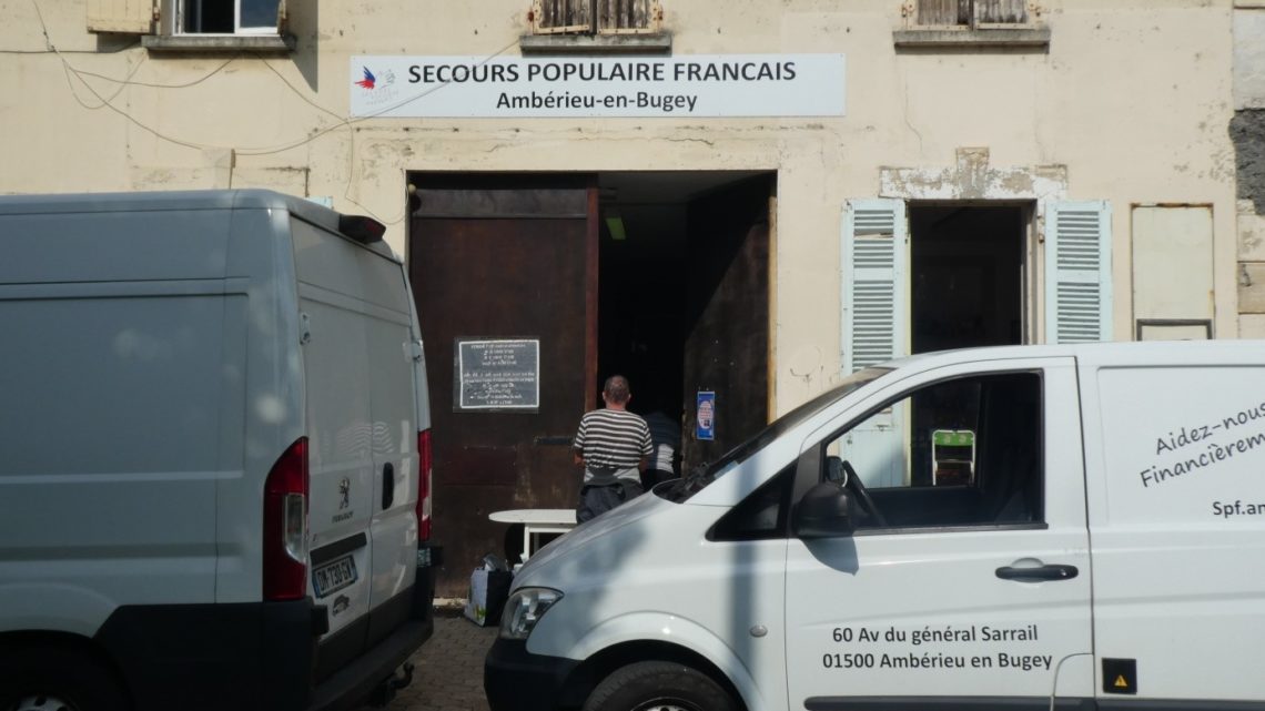 Entrée du Secours Populaire d'Ambérieu-en-Bugey, vu de la rue. Un homme au pull rayé est en train de passer la porte d'entrée.