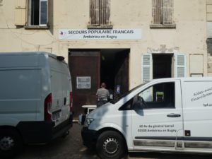 Entrée du Secours Populaire d'Ambérieu-en-Bugey, vu de la rue. Un homme au pull rayé est en train de passer la porte d'entrée.