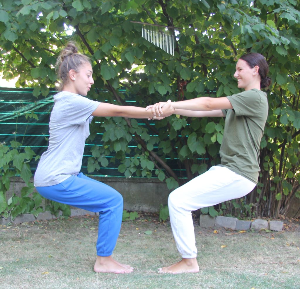 Aikido santé - posture : Deux jeunes filles se tiennent par les mains, face à face, en position de la chaise (assises dans le vide)