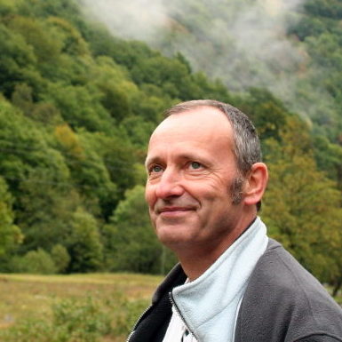 Portrait de Frantz Gacogne, un homme d'âge moyen souriant, dans un paysage naturel.