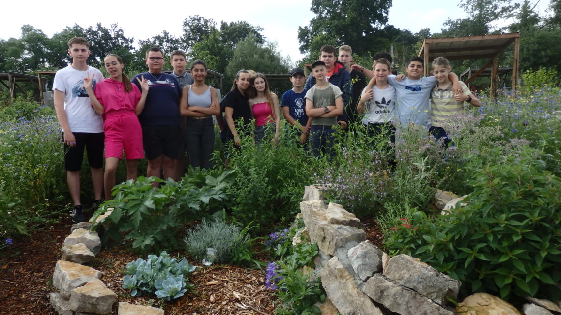 groupe d'une quinzaine de jeunes de l’ITEP des Alaniers, l’ITEP Seillon et l’Institut des jeunes sourds, fiers, posent au sein du jardin bucolique et différencié qu'ils ont créé devant des murets en pierres et plantes verdoyantes.