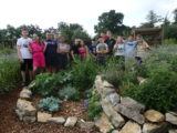 groupe d'une quinzaine de jeunes de l’ITEP des Alaniers, l’ITEP Seillon et l’Institut des jeunes sourds, fiers, posent au sein du jardin bucolique et différencié qu'ils ont créé devant des murets en pierres et plantes verdoyantes.