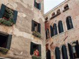 vue de deux bâtiments décrépis, une jeune fille et des plantes sont visibles aux fenêtres