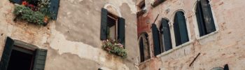 vue de deux bâtiments décrépis, une jeune fille et des plantes sont visibles aux fenêtres