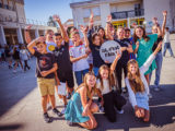 dans une cour de collège, un groupe d'enfants joyeux pose pour la photo avec un signe "Ici, c'est l'Ain"