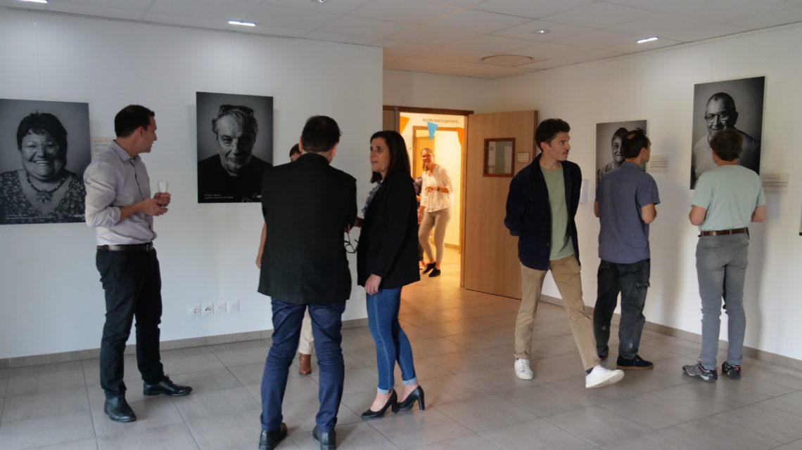 Vernissage de l'expo "Portraits de résidents" d'Alfa3a le 9 octobre 2023 : on voit les visiteurs discuter et regarder les tableaux dans la pièce d'exposition.