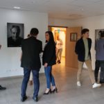Vernissage de l'expo "Portraits de résidents" d'Alfa3a le 9 octobre 2023 : on voit les visiteurs discuter et regarder les tableaux dans la pièce d'exposition.