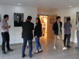 Vernissage de l'expo "Portraits de résidents" d'Alfa3a le 9 octobre 2023 : on voit les visiteurs discuter et regarder les tableaux dans la pièce d'exposition.