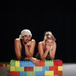 dans le cadre du festival inclusif L'iRrégulier, « Comme des enfants » est un spectacle pour tout public à partir de 14 ans. on voit sur l'image un homme et une femme sur scène, leurs coudes posés sur une construction d'enfant en briques colorées.