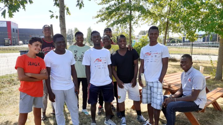 un groupe de jeunes migrants adolescents, mineurs non accompagnés (MNA) sourient pour la photo. ils sont dans un parc en été.